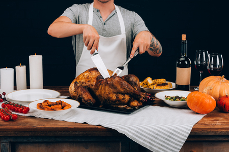 Man cutting baked turkey with fork and knife into pieces on thanksgiving dayの写真素材