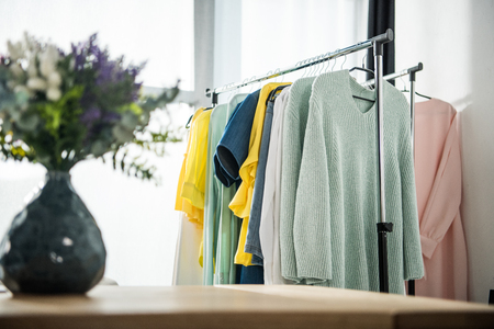 selective focus of vase with flowers and fashionable female clothes on hangersの写真素材