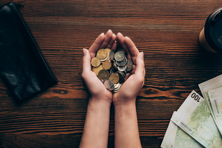 cropped view of female hands with coins, banknotes, wallet and coffee on wooden tabletopの写真素材
