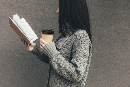 woman in sweater reading book and drinking coffee to go