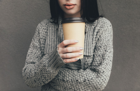 cropped view of woman in sweater holding disposable cup of coffeeの写真素材