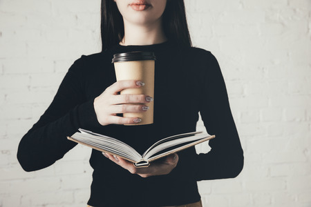cropped view of woman reading book and coffee to go