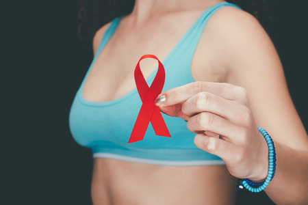 cropped view of woman in sport bra holding red aids ribbon, isolated on greyの写真素材