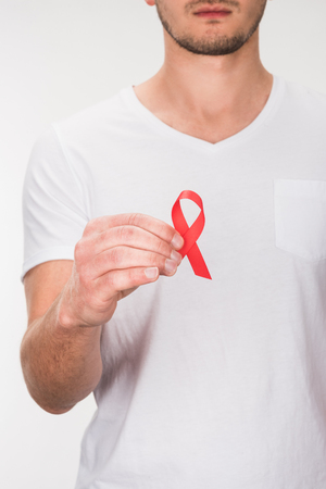 cropped view of man in white t-shirt holding red aids ribbon, isolated on white