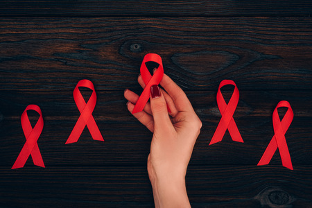 cropped view of female hand with red aids ribbons on wooden tabletop