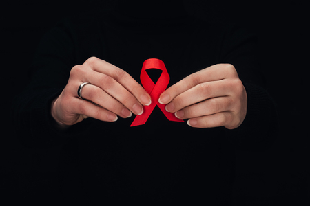 cropped view of woman holding red aids ribbon, isolated on blackの写真素材