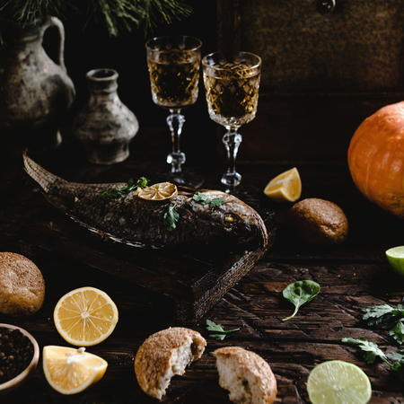 Baked fish with lemon and herbs on wooden board with white wine glasses
