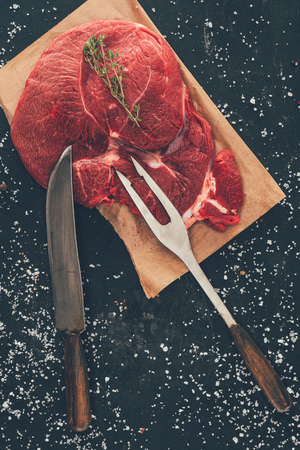 raw steak with fork and knife on wooden boardの写真素材