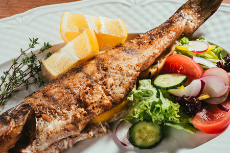 Baked fish with lemon and herbs on white plate