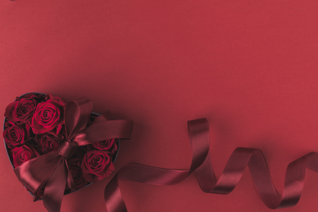 top view of roses in heart shaped gift box with ribbon isolated on red, st valentines day holiday conceptの写真素材
