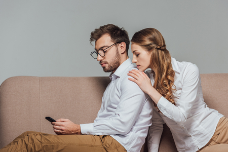 young woman looking at boyfriend using smartphone on sofaの写真素材