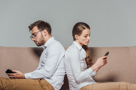 young couple sitting back to back and using smartphones