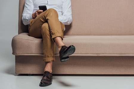 low section of young man using smartphone while sitting on sofaの写真素材