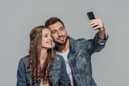 happy young couple in denim jackets taking selfie with smartphoneの写真素材