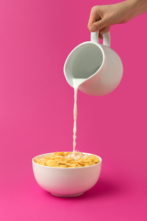 cropped shot of person pouring fresh healthy milk from jug into bowl with corn flakesの写真素材
