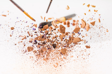 close-up shot of pieces of cosmetic powder with makeup brushes falling