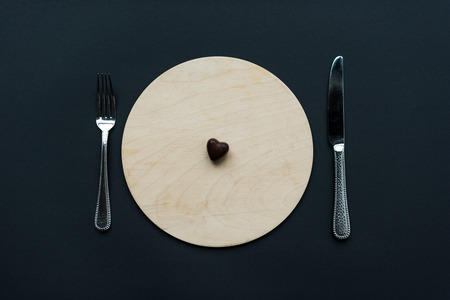 top view of heart shaped chocolate candy on round board with cutleryの写真素材