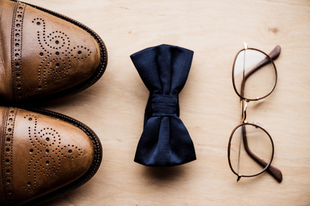 shoes, tie bow and glasses on wooden surface