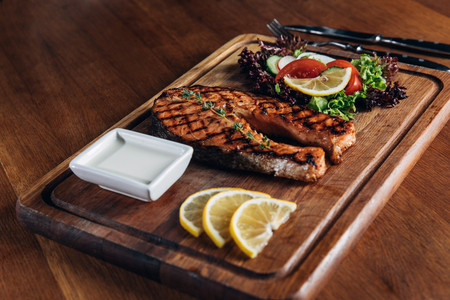 delicious grilled salmon steak served on wooden board with lemon and lettuceの写真素材