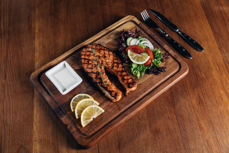 salmon steak served on wooden board with lemon and lettuceの写真素材