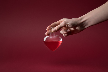 cropped image of woman holding heart shaped glass jar of love elixir isolated on redの写真素材