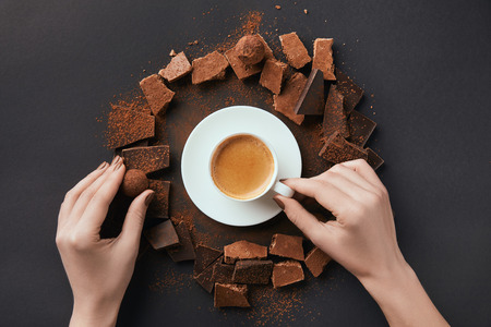 cropped shot of female hands, cup of coffee, truffles and chocolate on grey surfaceの写真素材
