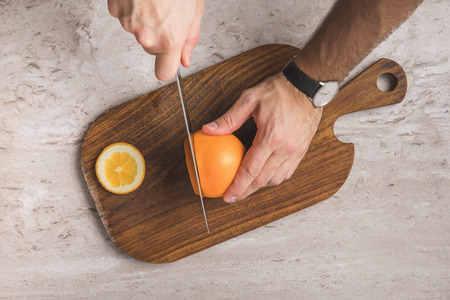 cropped image of man cutting orange on wooden board の写真素材