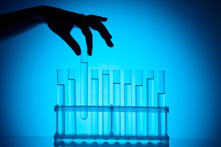 chemist taking glass tube from stand on blue