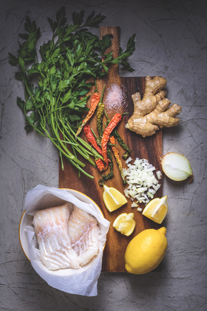 top view of raw fish in bowl, parsley, peppers, salt, onion, lemon and ginger