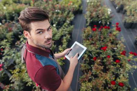 gardener in apron with tablet in hands looking at camera while working in gardenの写真素材