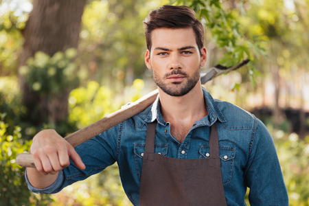 handsome gardener with spade on shoulder looking at camera in garden