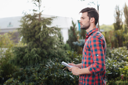 pensive gardener holding notebook in hands while standing in gardenの写真素材