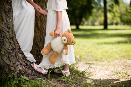 cropped shot of mother and daughter with teddy bear holding hands at park の写真素材