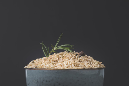 close-up shot of bowl of raw rice with rosemary and spices on black surface