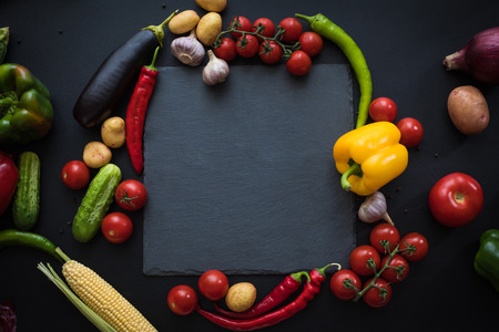 top view of various fresh ripe vegetables with slate board on blackの写真素材