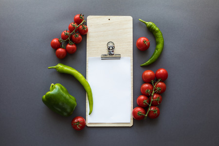 top view of various green peppers and ripe tomatoes with blank paper sheet on grey