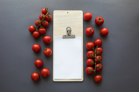 top view of fresh ripe tomatoes with blank paper sheet and cutting board on greyの写真素材