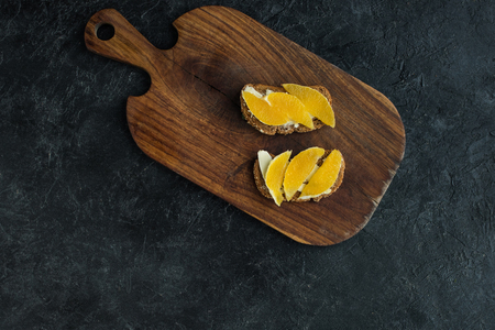 top view of snacks with orange pieces for breakfast on cutting board on dark surfaceの写真素材