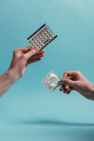 partial view of women holding condom and contraceptive pills in handsの写真素材