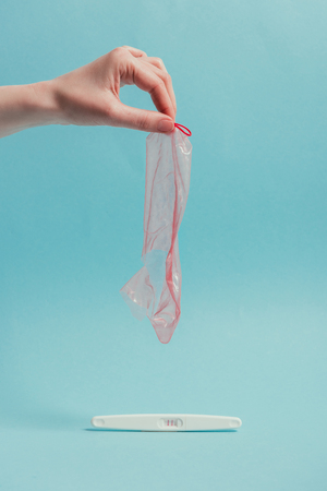 cropped shot of woman holding ripped condom in hand and pregnancy testの写真素材