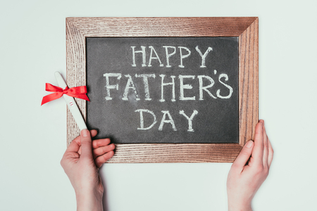 cropped shot of woman holding pregnancy test with ribbon and happy fathers day lettering on blackboardの写真素材