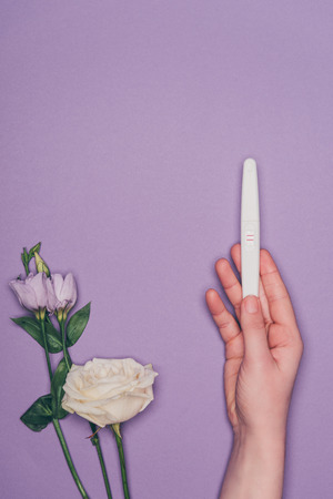 cropped shot of woman holding pregnancy test in hand and flowersの写真素材