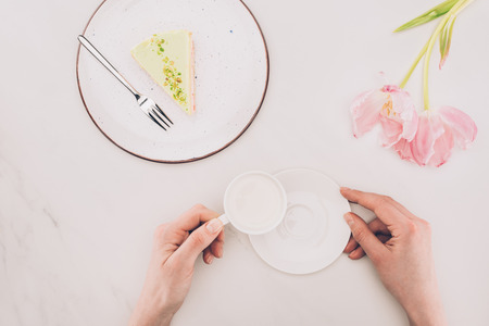 woman with cup of milk and piece of cake on plate on white surfaceの写真素材