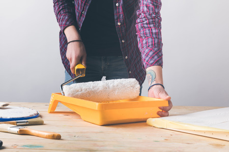 woman putting paint roll brush in white paint at wooden tableの写真素材