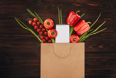 top view of red tomatoes and bell peppers with empty notebook on wooden tableの写真素材