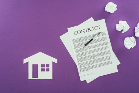 top view of business contract with pen and house symbol on purple surfaceの写真素材