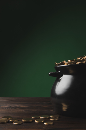 black pot of golden coins on wooden table on green, st patricks day conceptの写真素材