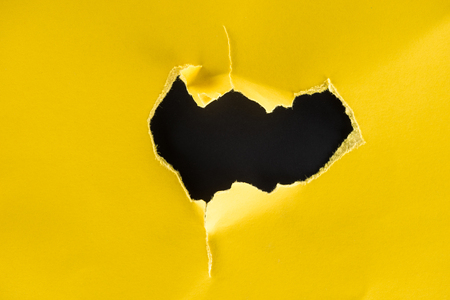 close-up shot of hole in yellow paper isolated on blackの写真素材