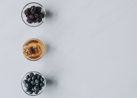 top view of glass bowls with berries and honey isolated on greyの写真素材