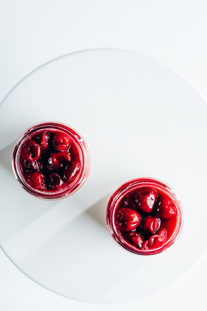 top view of sweet gourmet cherry dessert in glass jars on whiteの写真素材